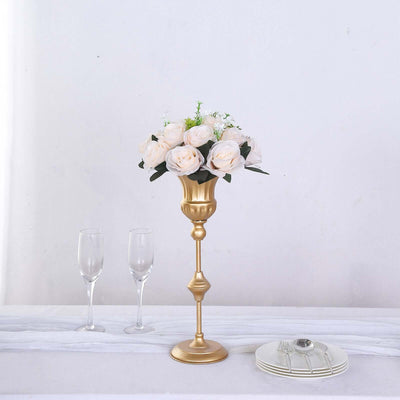 Gold flower vase with white roses, glass flutes, and a plate on a table.