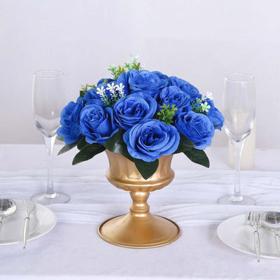 Blue rose arrangement in a gold vase on a dining table setting.
