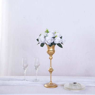 Gold candlestick vase with white roses and greenery on a table.