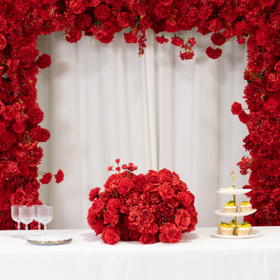Elegant red floral arrangement with tiered dessert stand on a table.