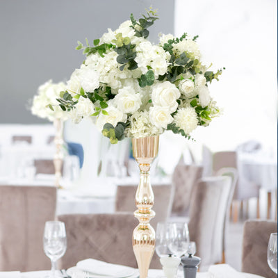 Elegant floral centerpiece with white roses and greenery in a gold vase.