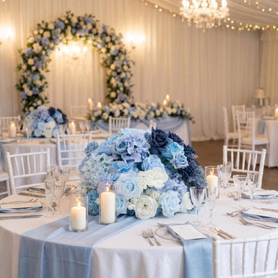 Elegant blue and white wedding reception table with floral centerpiece and candles