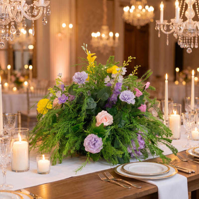 Elegant candlelit banquet table with pastel floral centerpiece and crystal chandeliers