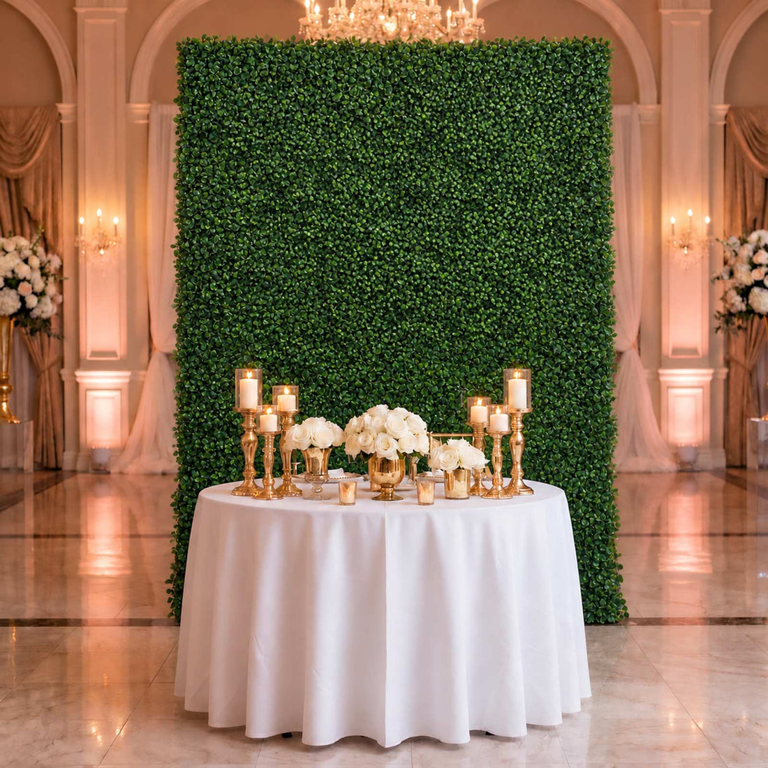 Elegant wedding reception backdrop with greenery wall, white roses, and gold candles