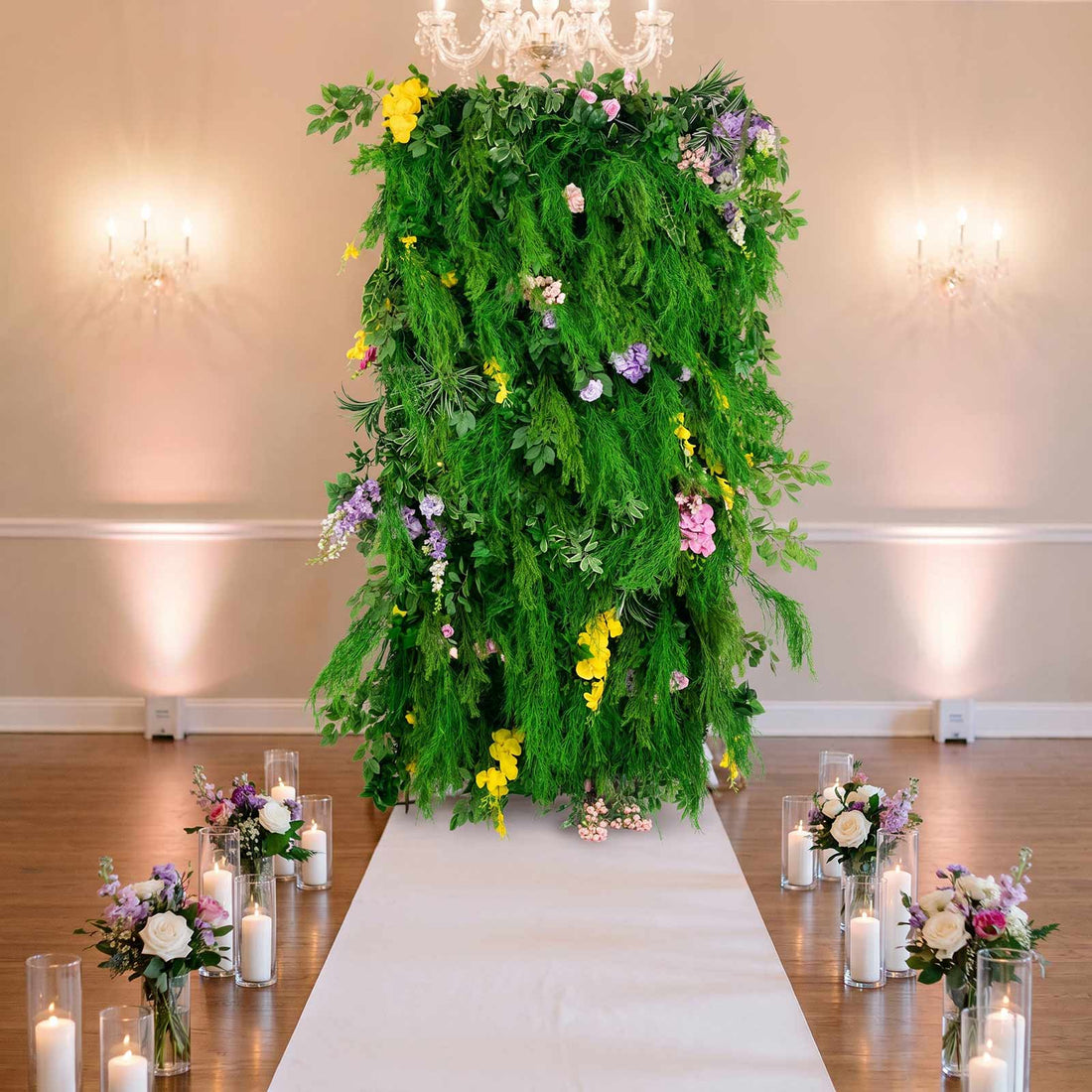 Elegant floral wedding arch with lush greenery, candles, and white aisle runner
