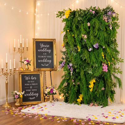 Wedding reception decor with floral greenery backdrop, candles, and gold frames