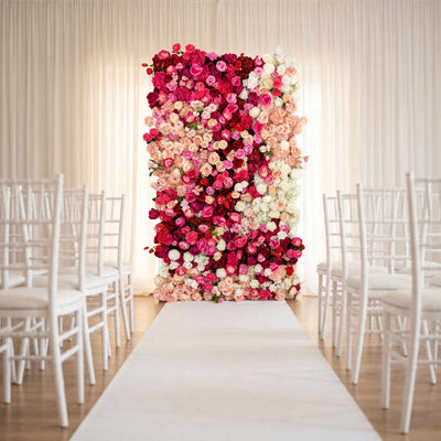 Wedding ceremony aisle with pink and white floral wall backdrop and white chairs