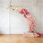 Curved floral arrangement in shades of pink and red against a white wall.