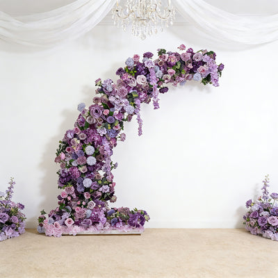 Floral arch arrangement in shades of purple against a white backdrop.