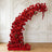 Red floral arch arrangement with roses and blooms against a decorative white wall.