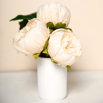 Artificial peony bouquet in a white vase against a neutral background.