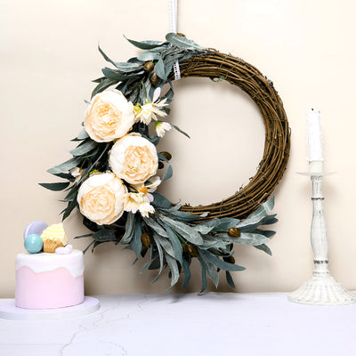Floral wreath with peonies and greenery beside a pastel cake on a table.