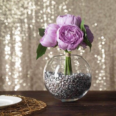 Purple peony flowers in a glass vase with decorative stones.