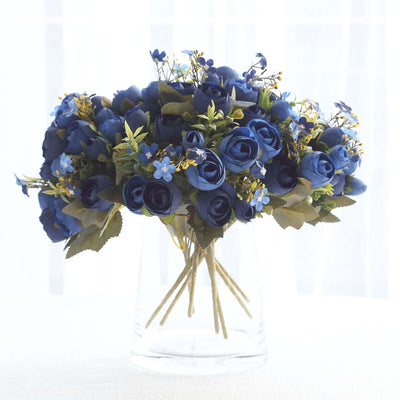 Blue floral bouquet in a clear glass vase on a light background.