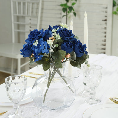 Blue floral arrangement in a glass vase on a table setting.