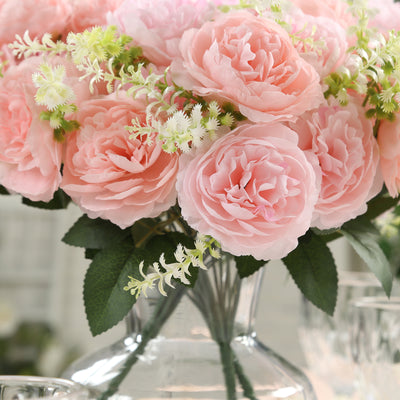Pink artificial roses in a clear vase with greenery.