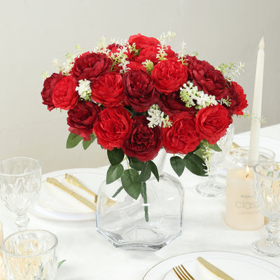 Red flower bouquet in a clear vase on a dining table setting.