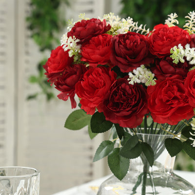 Artificial red rose bouquet in a clear vase with greenery.