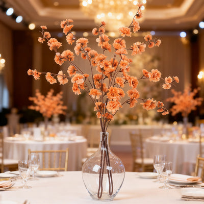Elegant orange flower arrangement in a glass vase for wedding decor.