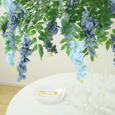 Artificial blue and green flowers hanging above a dining table setting.