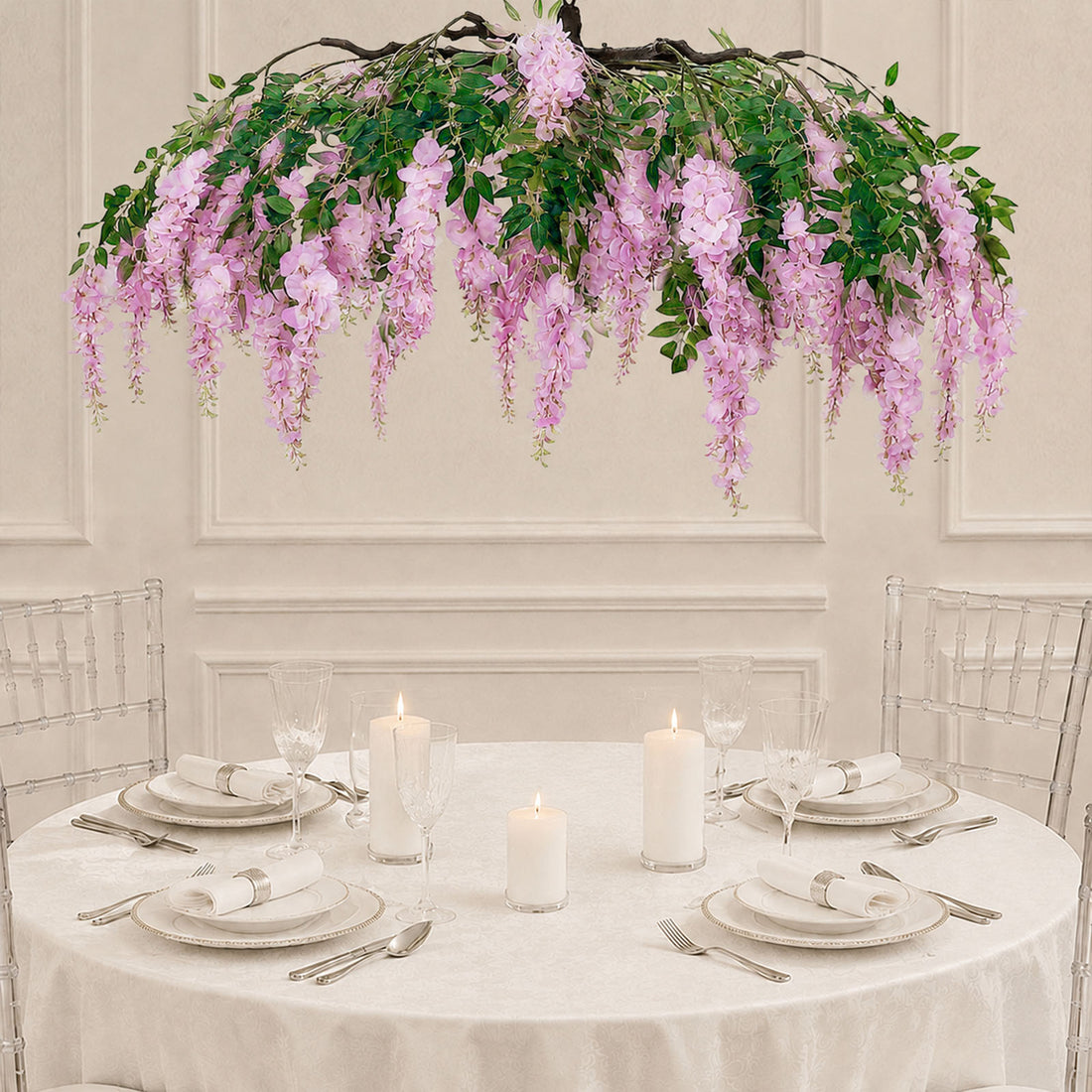 Elegant round table with white tableware, candles, and pink floral chandelier centerpiece