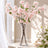 Pink cherry blossom arrangement in a clear glass vase on a sunlit table