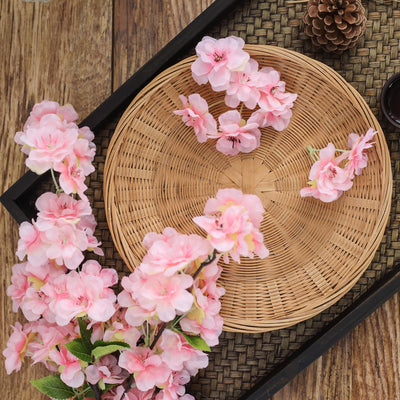 Pink silk cherry blossoms arranged on a woven tray.