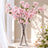 Pink cherry blossom arrangement in a clear glass vase by a sunlit window