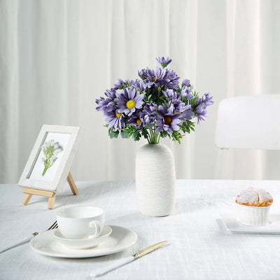Purple floral arrangement in a textured vase on a dining table.