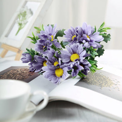 Purple faux flowers arrangement on a magazine with a coffee cup.