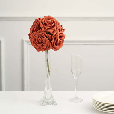 Artificial orange rose bouquet in a glass vase with a champagne flute and plates.