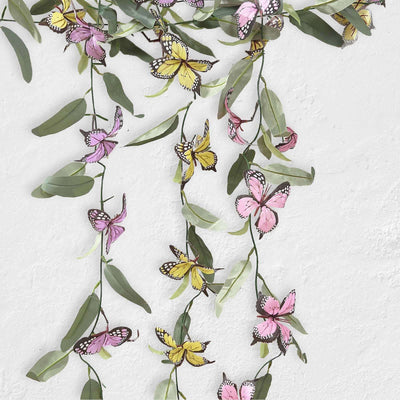Colorful butterfly and leaf garland decoration on a white wall.