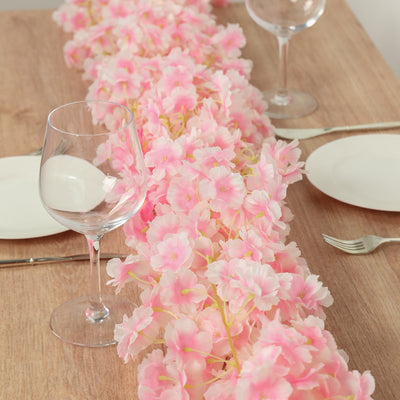 Pink floral table runner with wine glasses and plates on a wooden table setting.