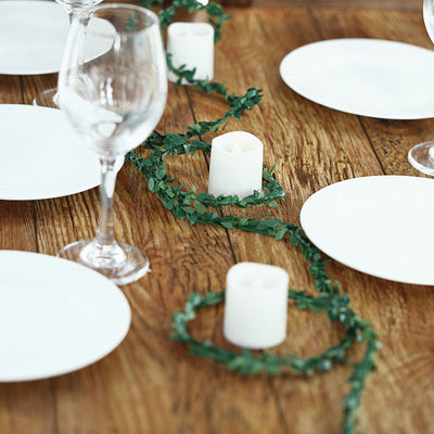 Elegant table setting with candles and greenery on a rustic wooden surface.