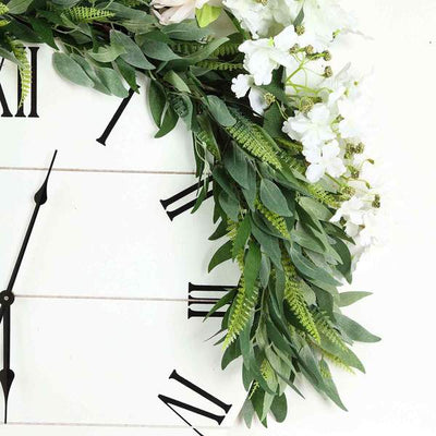 Floral wall clock with greenery and white flowers on a rustic wooden background.