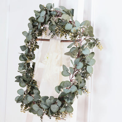 Eucalyptus wreath hanging on a ladder against a white wall.