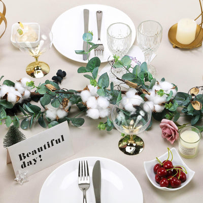 Elegant table setting with greenery, cotton accents, and decorative elements.