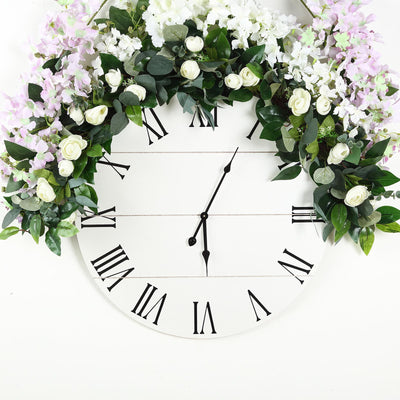 Floral wall clock with Roman numerals and greenery decoration.