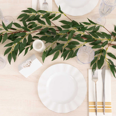 Elegant table setting with white plates and greenery decor.