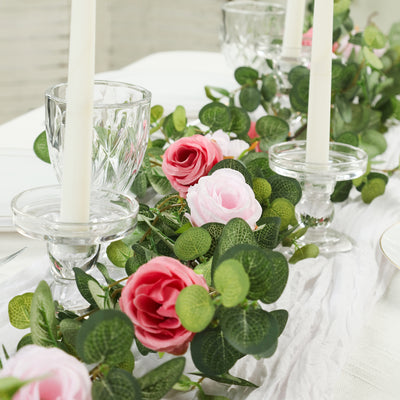 Floral table centerpiece with pink roses and greenery, featuring candles.