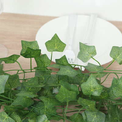 Artificial ivy leaves on a wooden table with a plate and cutlery in the background.
