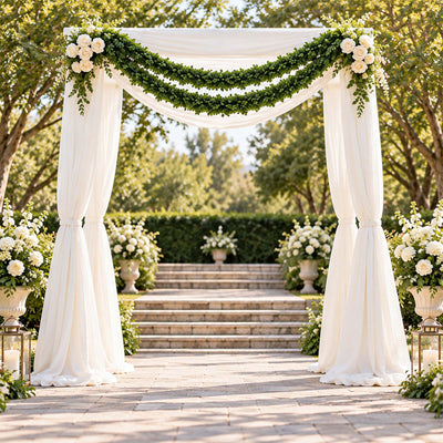 Elegant outdoor wedding arch with white drapes, greenery, and white roses