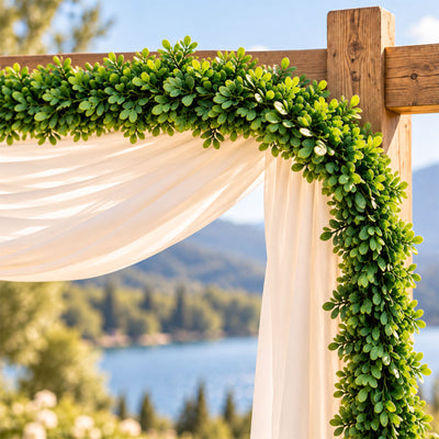 Greenery and white drapery decorating a rustic outdoor wedding arch by the lake