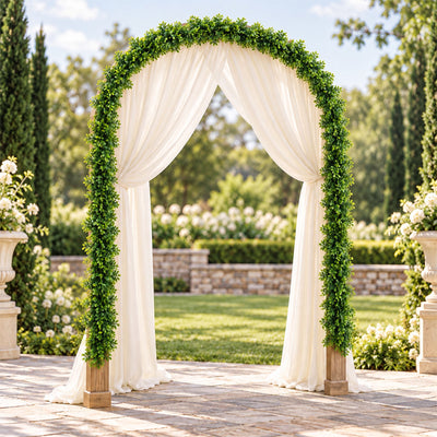 Outdoor wedding arch with greenery and white drapes in garden setting