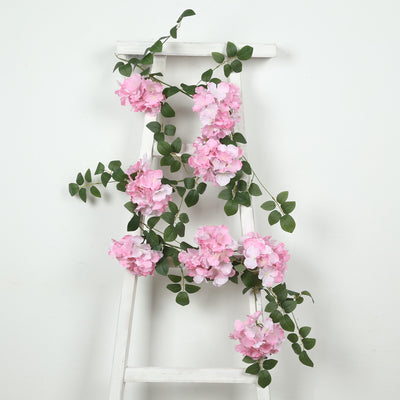 Pink artificial flower garland on a white ladder against a plain background.