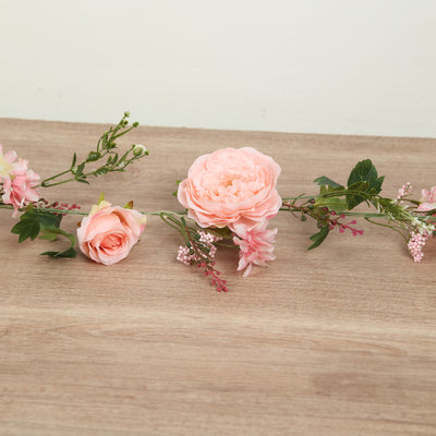 Pink floral arrangement with peonies and greenery on wooden surface.