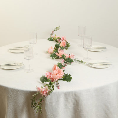 Floral table centerpiece with pink flowers and greenery on a dining table.