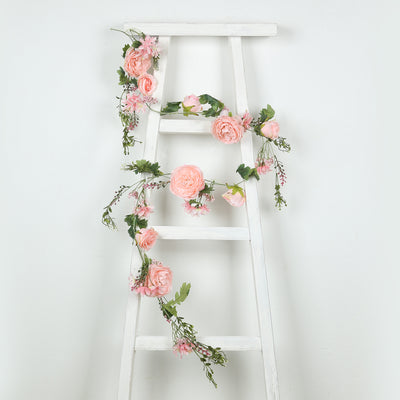 Floral garland draped on a white ladder with pink roses and greenery.