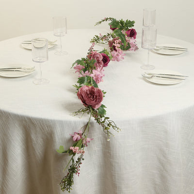Floral table runner with pink and purple flowers on a white table setting.