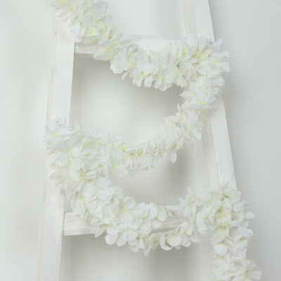 White floral garland draped on a white ladder against a plain backdrop.